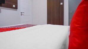 A bedroom with a white bed, a red and white patterned blanket, a wooden door, and a dark wooden wardrobe. - Super OYO 90115 Near Pasar Baru (Jakarta)