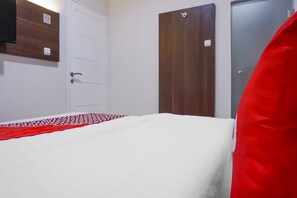 Un dormitorio con una cama blanca, un edredón blanco y rojo estampado, una puerta de madera y un armario de madera oscura.