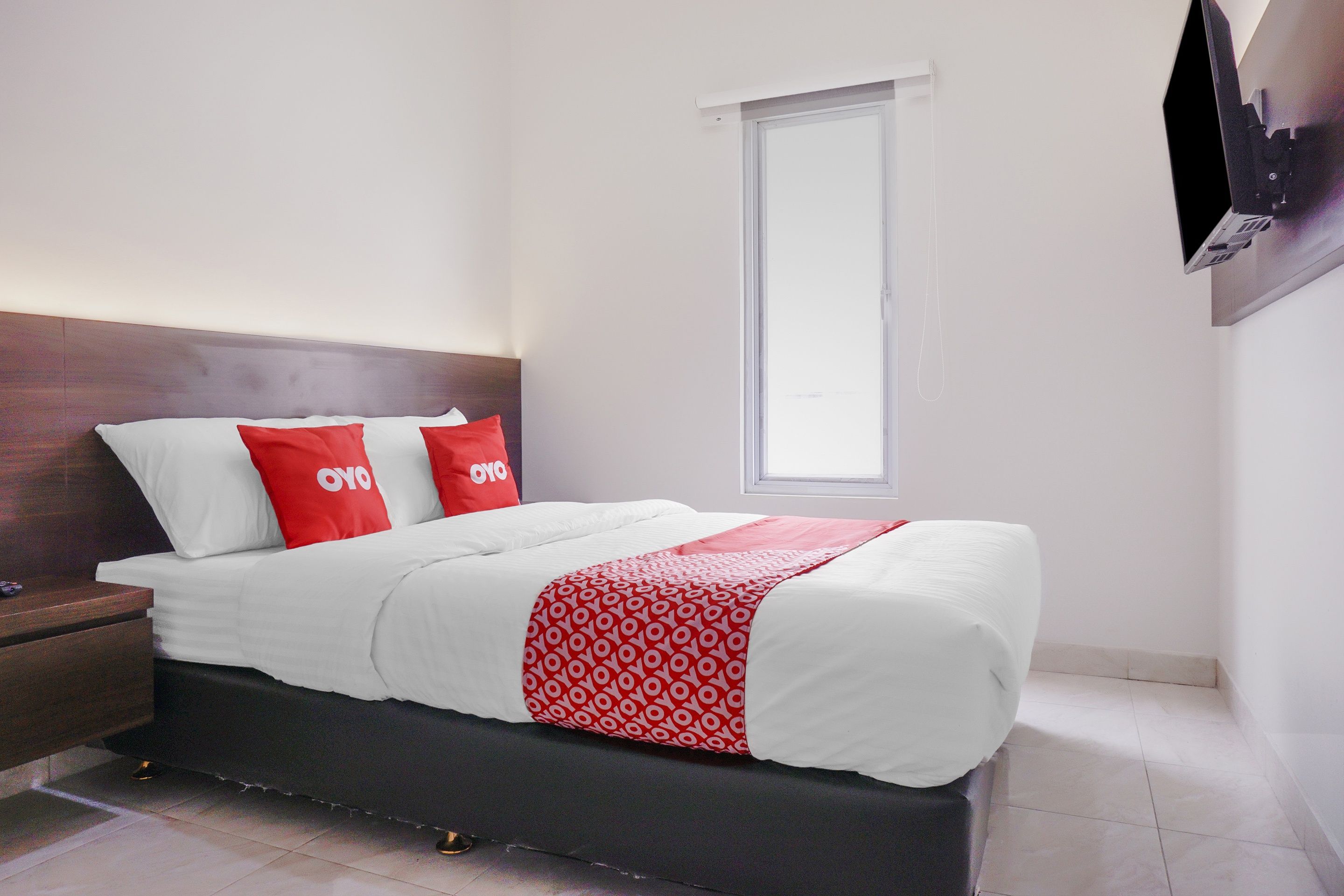 Una cama bien hecha con ropa de cama blanca y roja, un cabecero de madera y una mesita de noche con una lámpara.
