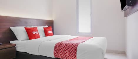 Una cama bien hecha con ropa de cama blanca y roja, un cabecero de madera y una mesita de noche con una lámpara.