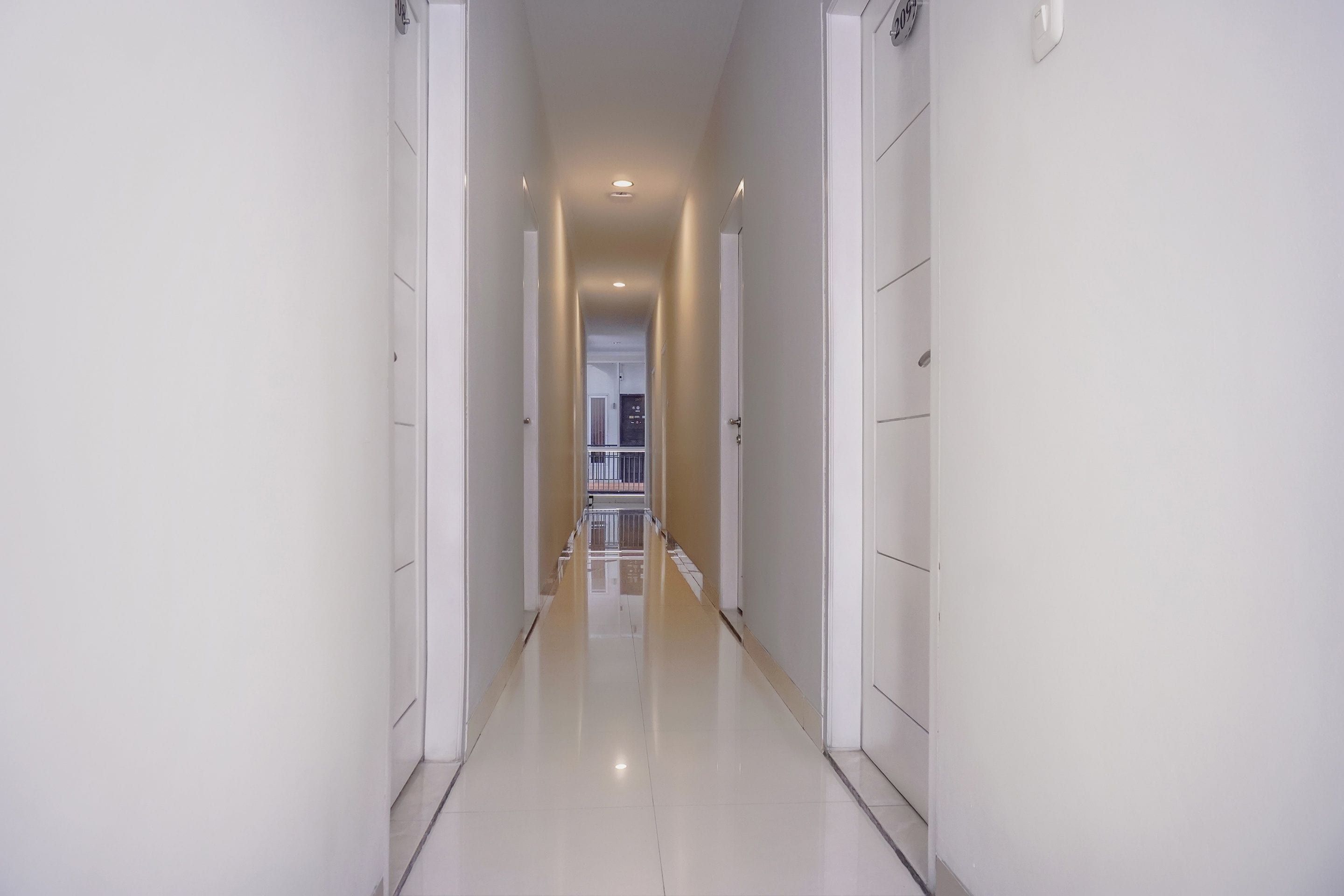 A long, narrow hallway with white walls and a shiny floor, leading to a door at the end.