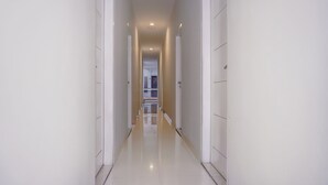 A long, narrow hallway with white walls and a shiny floor, leading to a door at the end. - Super OYO 90115 Near Pasar Baru (Jakarta)
