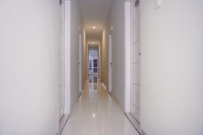 Un pasillo largo y estrecho con paredes blancas y un suelo brillante, que conduce a una puerta al final.