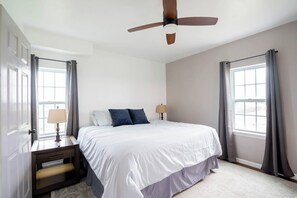 A bedroom with a bed, bedside tables, a ceiling fan, and large windows with curtains.