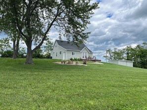 A white house with a sloped roof, surrounded by a well-maintained lawn and a large tree.