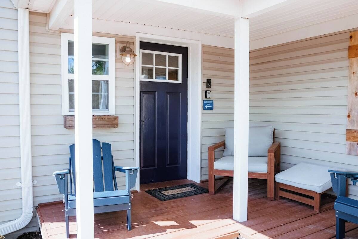 Une véranda avec deux chaises bleues et un banc en bois doté de coussins.