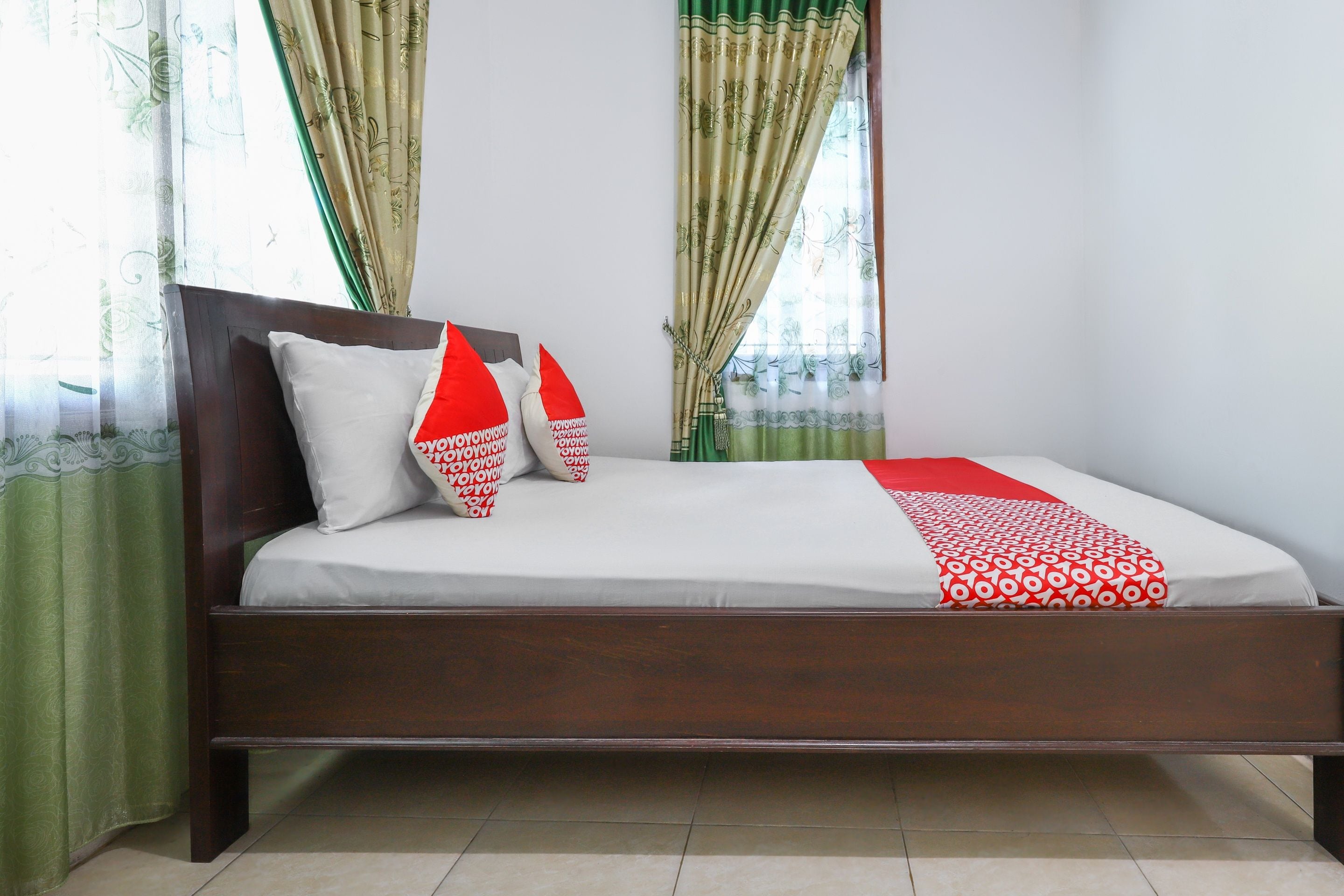 A standard hotel room with a single bed, a wooden headboard, and green curtains.