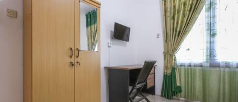 A room with a wooden wardrobe, a desk with a chair, a television, and green curtains.