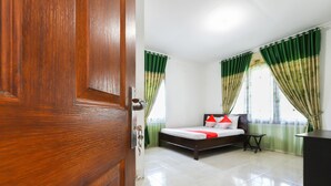 A hotel room with a wooden door, a bed with a red and white bedspread, green curtains, and a small table. - OYO 3789 Bukit Somber Residence Syariah (Balikpapan)