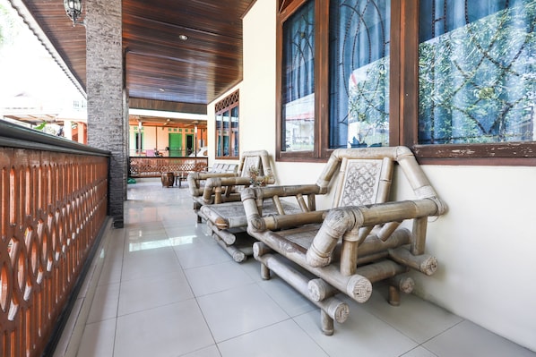 A corridor with a tiled floor, wooden benches, and a view of a building with green doors.