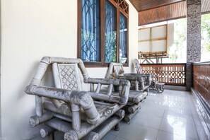 Un banc en bois traditionnel orné de sculptures complexes, un tapis tissé et un vase décoratif rempli de fleurs.