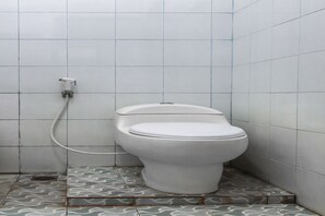 Un baño pequeño con azulejos, un inodoro y una tubería visible.
