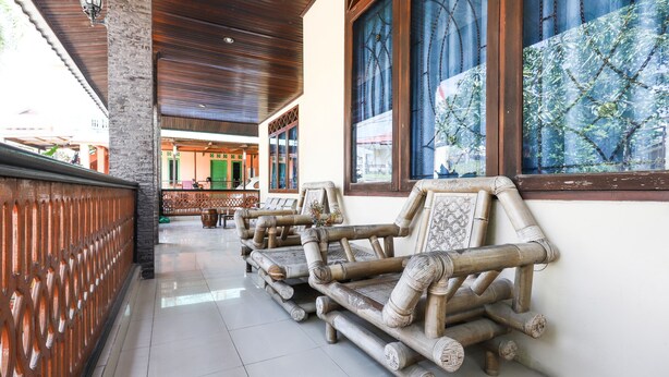 A corridor with traditional bamboo furniture, a tiled floor, and a view of a building with green doors. - OYO 3789 Bukit Somber Residence Syariah (Balikpapan)