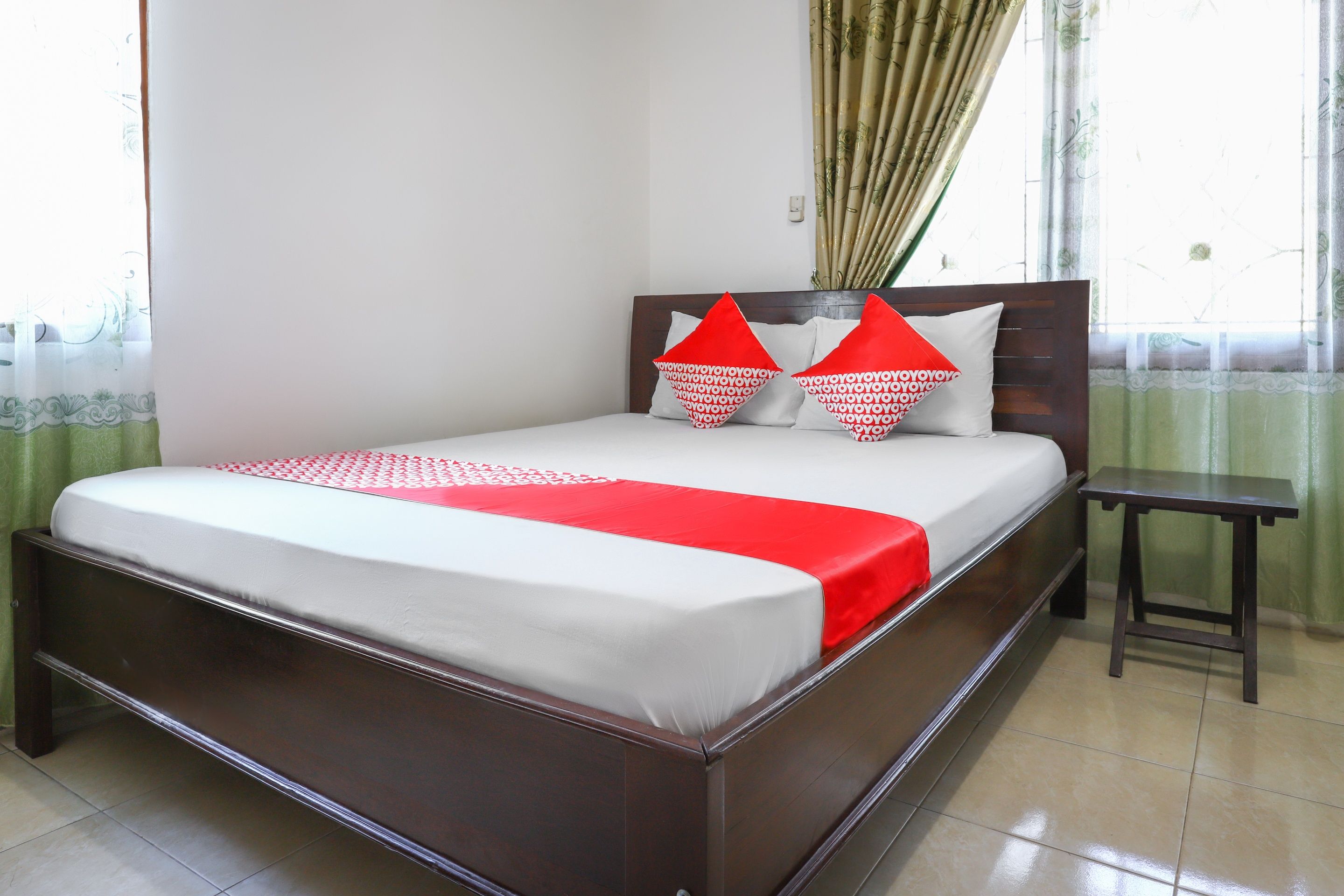 A neatly made bed with a red and white bedspread, two pillows with red and white patterns, and a small wooden nightstand beside the bed.