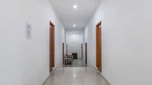 A clean, well-lit hallway with white walls and a tiled floor, leading to a room with a bed and a desk. - OYO 3789 Bukit Somber Residence Syariah (Balikpapan)