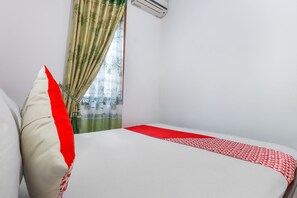 A room with a bed, a pillow, a window with curtains, and an air conditioning unit. - OYO 3789 Bukit Somber Residence Syariah (Balikpapan)