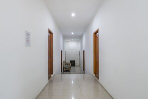 Un couloir propre et bien éclairé, avec des murs blancs et un sol carrelé, qui mène à une pièce contenant un lit et un bureau.