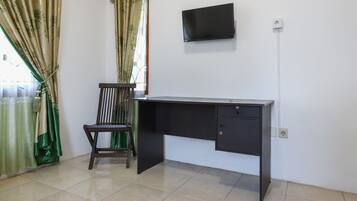 Una habitación con escritorio, silla, televisor montado en la pared y ventana con cortinas.