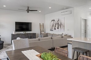 A modern living room with a sectional sofa, a dining table, and a flat-screen TV.
