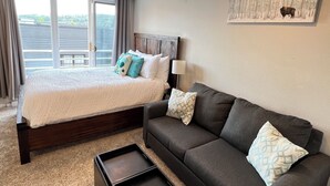 A bedroom with a bed, a dark sofa, a small table, and a painting on the wall.