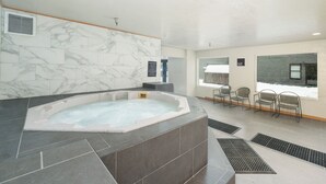 A spa area with a hot tub, marble walls, and seating by a window.