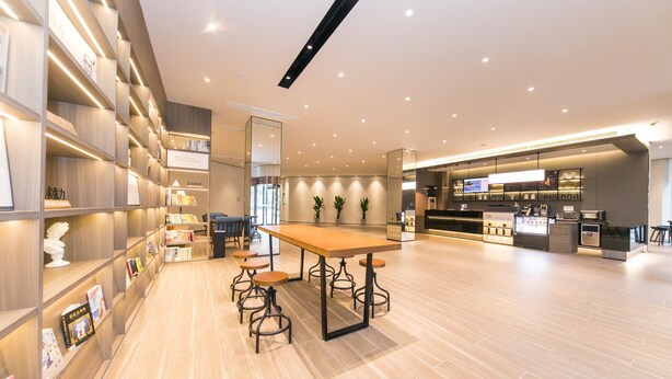 A modern interior with wooden shelves, a central table with stools, and a kitchen area. - Hanting Hotel Taizhou Jiaojiang Baolong City (Taizhou)