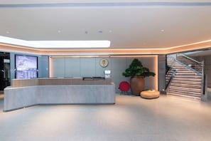 A modern reception area with a curved reception desk, a digital display, a potted plant, a red chair, and a staircase. - Ji Hotel Shanghai People's Square Fujian Middle Rd (Shanghai)