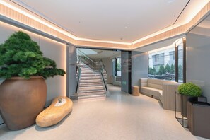 Un interior moderno con una escalera, una planta grande en maceta, un banco de madera y un sofá.