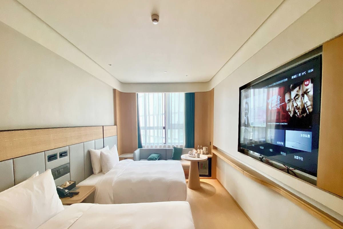 Habitación de hotel con dos camas, un televisor en la pared, una mesita y una ventana con cortinas.