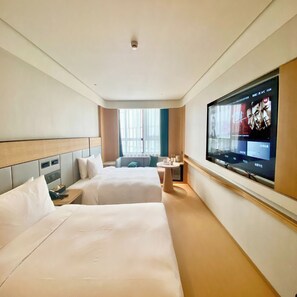 A hotel room with two beds, a TV on the wall, a small table, and a window with curtains.