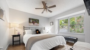 Une chambre à coucher avec un lit, des lampes de chevet, un ventilateur de plafond, une fenêtre donnant sur l’extérieur et un banc placé près de la fenêtre.