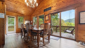 L’intérieur d’un chalet en bois, avec une table et des chaises, un lustre et une vue sur l’extérieur.