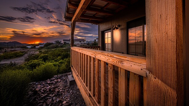 A wooden balcony with a view of the sunset and surrounding landscape.