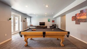 A pool table in a room with a sofa, a television, and artwork on the walls.