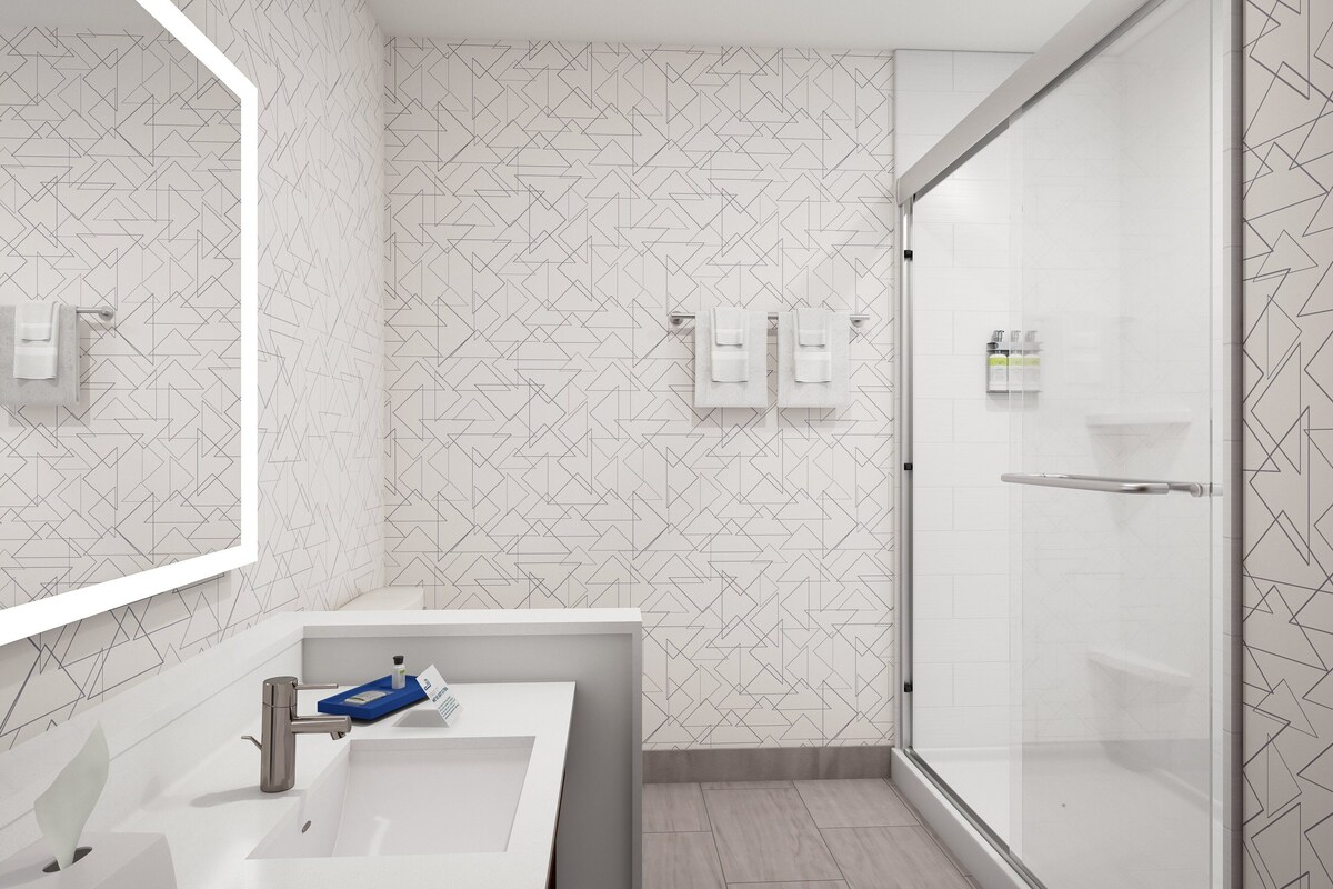 A modern bathroom with a geometric patterned wall, a white sink with a blue soap dish, and a glass shower enclosure.