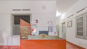 A reception area with a desk, a clock, a calendar, and a window with a metal grill.