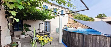 A backyard with a pool, a pergola, a table with chairs, and a potted plant.