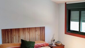 Une chambre à coucher avec une tête de lit en bois, un lit avec plusieurs oreillers, une table de chevet avec une lampe et une fenêtre avec des stores.