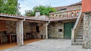 Une cour bordée de murs en pierre, surmontée d’un toit en tuiles et dotée d’un escalier menant à un niveau supérieur.