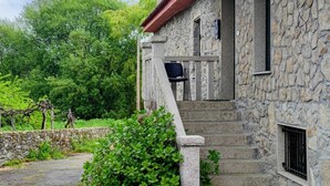 Un bâtiment en pierre avec un toit rouge, un escalier menant à un balcon et une vue sur une végétation luxuriante.