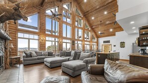 A spacious living room with a large gray sectional sofa, a leather couch, and a stone fireplace. - Beautiful Views from the Rusty Moose (Branson West)