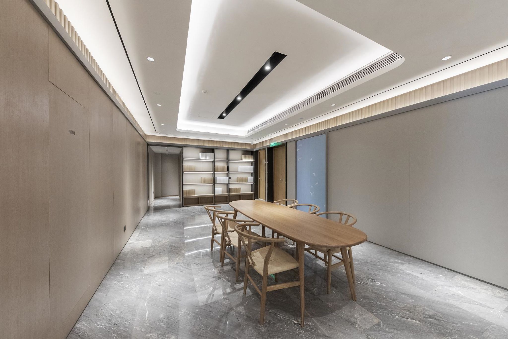 A modern conference room with a long table, chairs, and a bookshelf in the background.