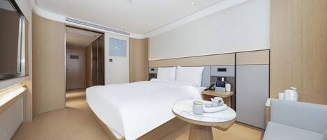A modern hotel room with a large bed, a bedside table with a lamp, a small round table with a cup and saucer, and a chair.