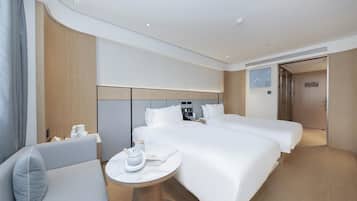 A hotel room with two beds, a small table with a kettle, a chair, and a wooden headboard.