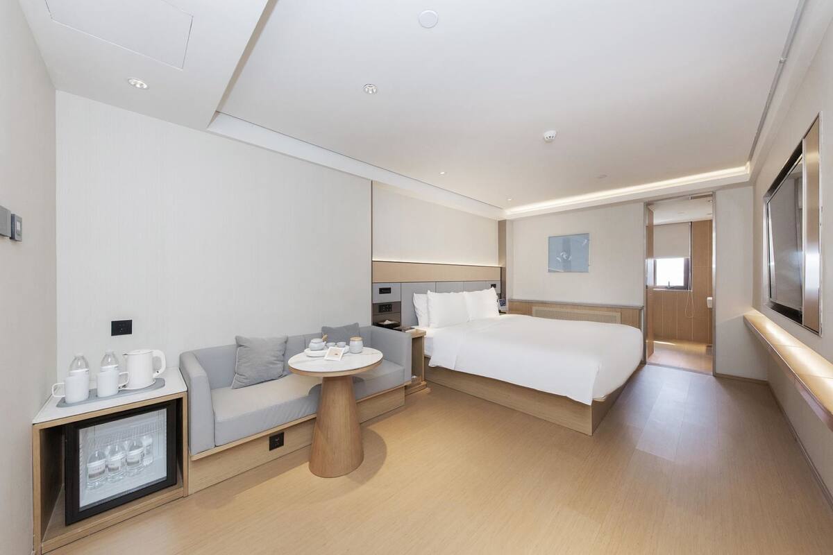 Una habitación de hotel moderna con cama, sofá, mesita de noche y televisión.