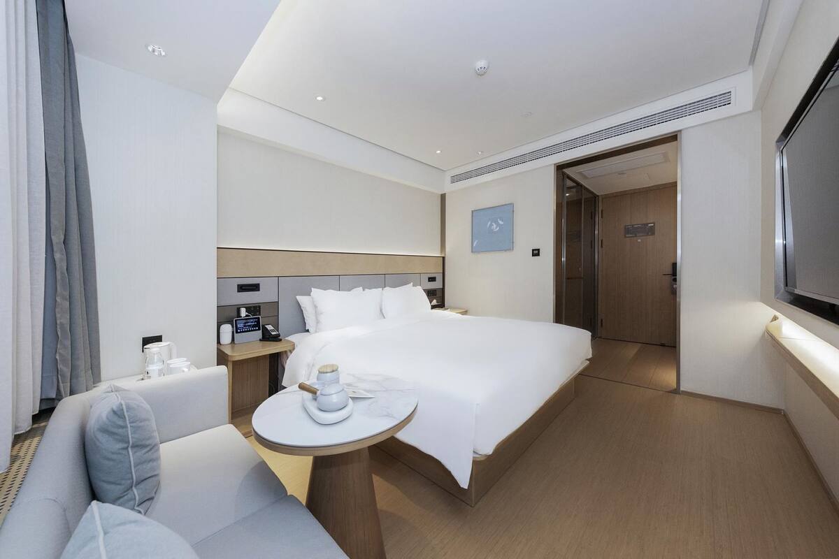 Una habitación de hotel moderna con una cama grande, una mesita con una taza, un sofá y un televisor.