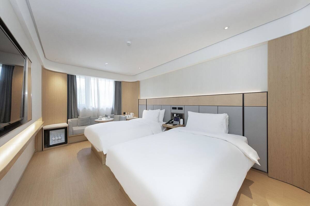 Una habitación de hotel moderna con dos camas, un sofá, una mesita y un televisor.