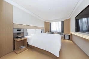 A modern hotel room with a large bed, bedside tables, a small desk, and a window with curtains.
