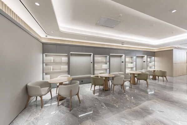 A modern interior with marble flooring, round tables, and chairs, and built-in shelving units.