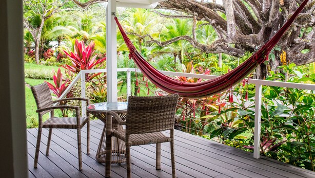 Eine Holzterrasse mit Korbstühlen und einem Tisch, einer roten Hängematte und üppiger tropischer Vegetation.
